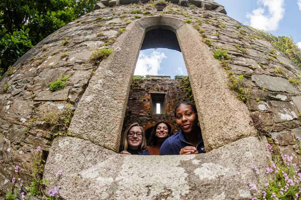 three female students looking out a historic stone wall window