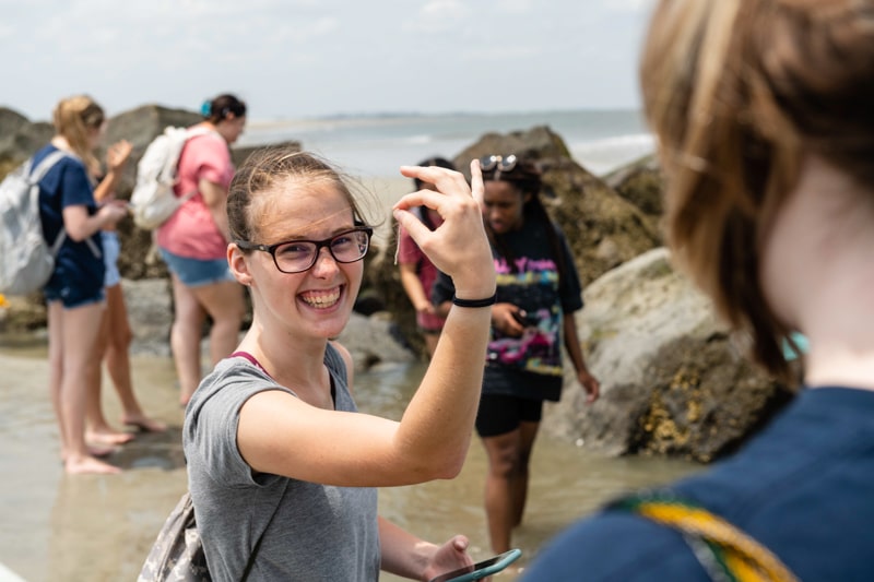 female student holding up something found in the tide pools at tybee island with a large smile on her face